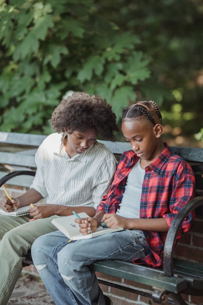 Two teenagers studying on a park bench with notebooks, outdoors education.